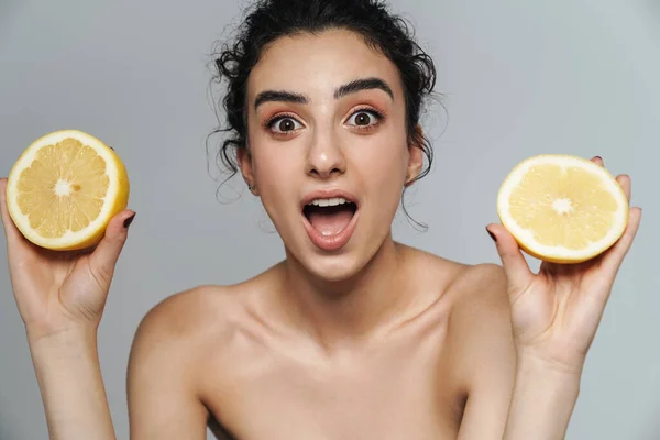 興奮した半裸の女がグレーの壁に隔離されたレモンでポーズをとりながら驚きを表現 — ストック写真