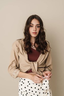 Kumral saçlı, bej rengi duvarın üzerinden izole edilmiş kameraya bakan güzel bir kadın resmi.