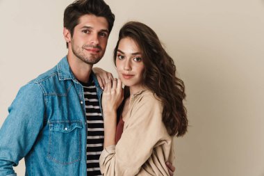 Bej arka planda izole edilmiş genç ve güzel bir çiftin kucaklaşması ve poz vermesi.