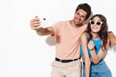 Beyaz arka planda izole edilmiş akıllı telefondan selfie çekilirken gülümseyen mutlu çiftin görüntüsü