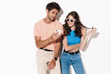 Beyaz arka planda izole edilmiş cep telefonuyla poz veren çekici genç bir çift