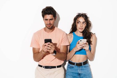 Beyaz arka planda izole edilmiş cep telefonlarıyla poz veren odaklanmış genç bir çift görüntüsü
