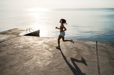 Kulaklıklı Afro-Amerikalı genç bir kızın beton gezinti güvertesinde koşuşunu hayal et.