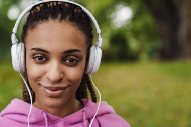 Parkta kulaklıkla müzik dinleyen çekici, genç bir Afrikalı spor kadınını yakından çek.