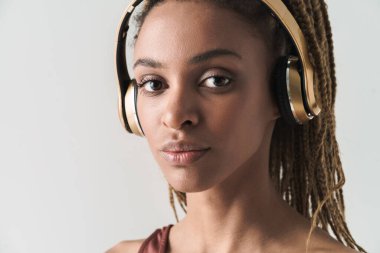 Güzel gülümseyen Afrikalı esmer kadının portresini yakından çek. Rastalı esmer kadın. Beyaz arka planda izole edilmiş kablosuz kulaklıklarla müzik dinliyor.