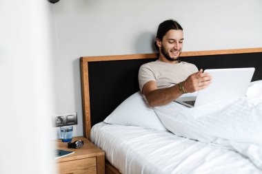 Sabah yatak odasında dizüstü bilgisayarıyla çalışan mutlu bir adam.