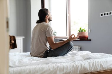 Genç adam sabahları yatak odasında meditasyon yapıyor.