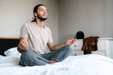 Genç adam sabahları yatak odasında meditasyon yapıyor.