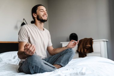 Genç adam sabahları yatak odasında meditasyon yapıyor.
