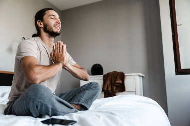 Genç adam sabahları yatak odasında meditasyon yapıyor.