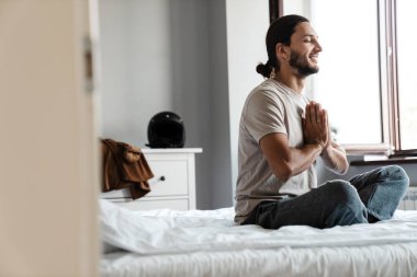 Genç adam sabahları yatak odasında meditasyon yapıyor.