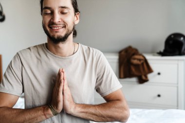 Genç adam sabahları yatak odasında meditasyon yapıyor.