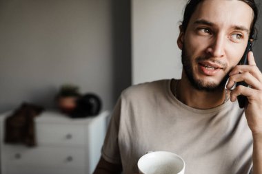 Çekici, gülümseyen, cep telefonu kullanan, elinde bardak tutan genç adam.