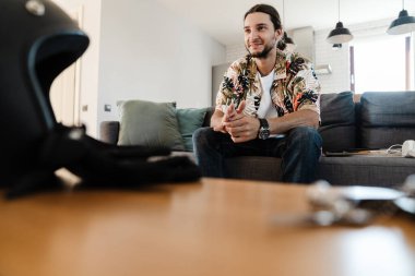 Evde televizyon izleyen, kanepede oturan gülümseyen genç adam.