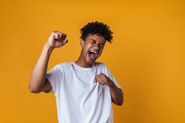 Heyecanlı bir Afrikalı Amerikalı 'nın sarı duvardan izole bir şekilde bağırıp, kazanan jestler yapması.