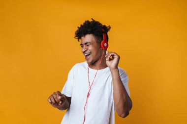 Heyecanlı Afrikalı Amerikalı bir adamın görüntüsü. Kulaklıklı müzik dinliyor ve sarı duvarın üzerinde dans ediyor.
