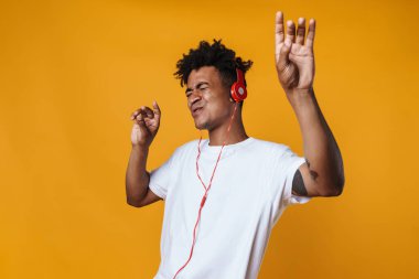 Heyecanlı Afrikalı Amerikalı bir adamın görüntüsü. Kulaklıklı müzik dinliyor ve sarı duvarın üzerinde dans ediyor.