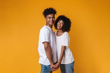 Mutlu Afrika kökenli Amerikalı bir çiftin el ele tutuşup gülümsemesi sarı duvarın ardında izole edilmiş.