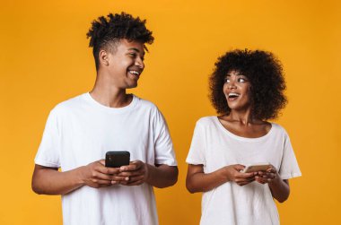 Sarı arka planda izole edilmiş cep telefonlarıyla gülen ve kullanan Afro-Amerikan vatandaşlarının fotoğrafı.