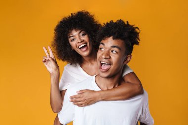 Afrika kökenli Amerikalı bir çiftin sarı duvarın üzerinde tek başına at sürerken barış işareti yapması.