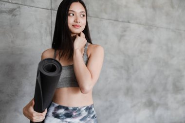 Evde yoga minderiyle poz veren Asyalı güzel bir kız resmi.