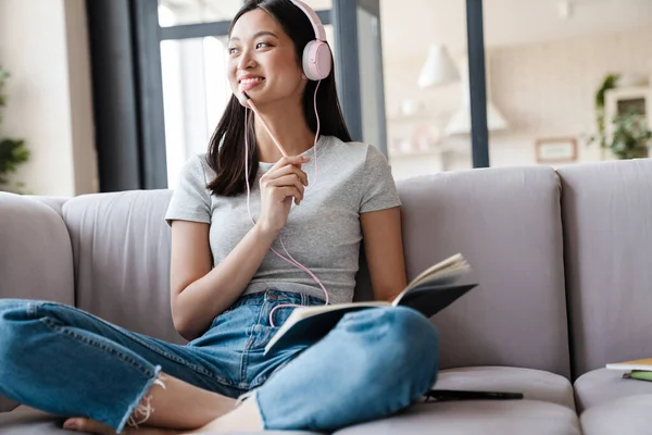 Imagen Una Mujer Asiática Sonriente Usando Auriculares Anotando Notas Mientras —  Fotos de Stock