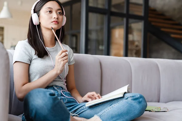 Imagen Mujer Asiática Enfocada Usando Auriculares Anotando Notas Mientras Está —  Fotos de Stock