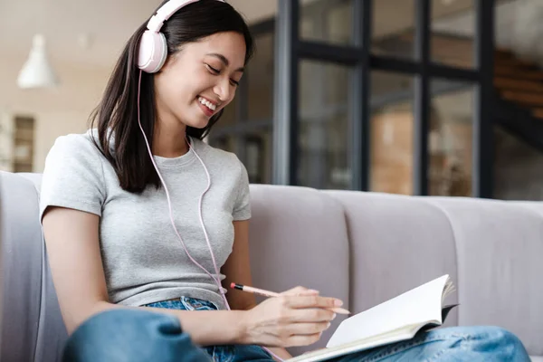 Bild Einer Lächelnden Asiatischen Studentin Mit Kopfhörer Die Notizen Aufschreibt — Stockfoto