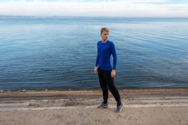 Spor giyim genç adam'ın kıyısında duruyor. Sabah erken.