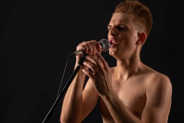 Topless kaveri laulaa punk rockia mikrofonissa tummalla taustalla — kuvapankkivalokuva