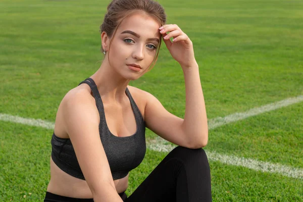 Sexy atletische meisje zittend op gras in een stadion — Stockfoto