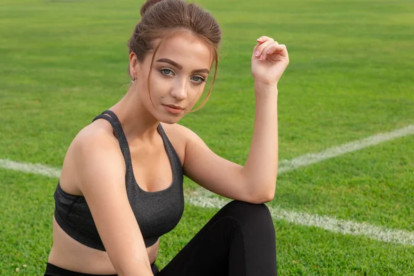 Szexi sportos lány ül a fűben a stadionban — Stock Fotó