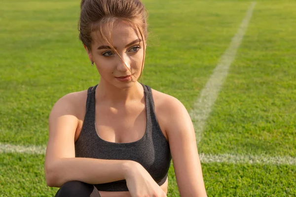 Fille athlétique sexy assis sur l'herbe dans un stade — Photo