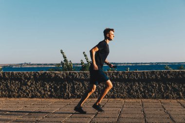 Genç adam gün doğumunda parkta koşuyor..