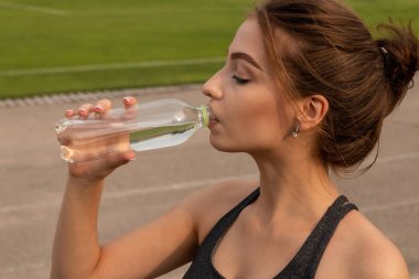 Genç seksi atletik kız içecekler su, bir stadyum üzerinde ayakta.