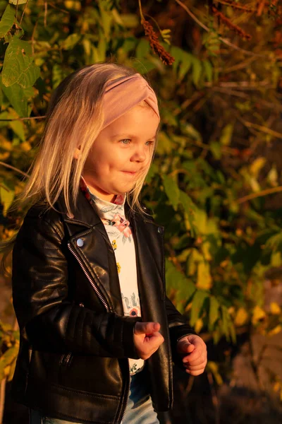 Liten flicka i en läderjacka, spelar i parken hösten. — Stockfoto