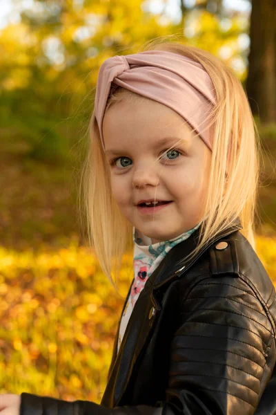 Klein meisje in een leren jas, spelen in het najaar park. — Stockfoto