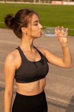 Genç seksi atletik kız içecekler su, bir stadyum üzerinde ayakta.