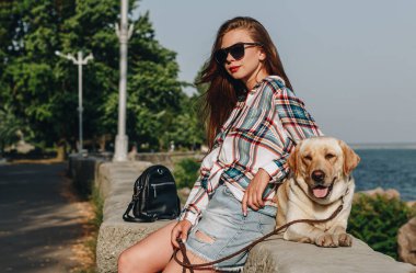 Açık havada uzun saçlı güzel bir kızın bir köpekle gezerken çekilmiş bir resmi..