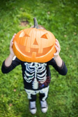 Çocuk pupmkin Cadılar Bayramı'nda tutan iskelet kostüm
