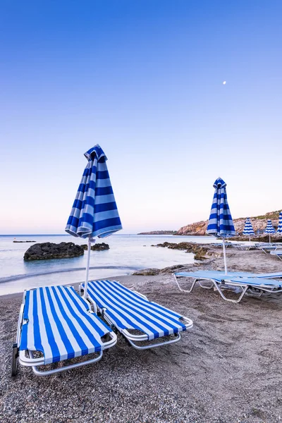 Tipici lettini prendisole sulla spiaggia di ghiaia selvaggia di Rodi, Grecia a Sunri — Foto Stock