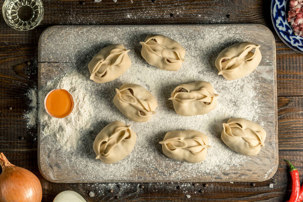 Узбекская национальная пищевая манта, как пельмени, на деревянной доске, лежит в муке с яйцом. Горизонтальная рамка
