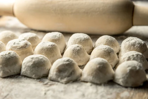 Uzbek national food Chuchvara, like dumplings, with a rolling pin, on a wooden board, in flour. Horizontal frame