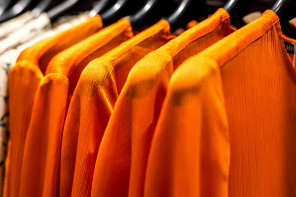 Orange clothes hanging on store racks. Horizontal frame