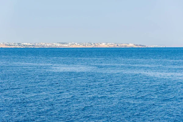 hotels and houses in the distance stand over a cliff above the blue sea