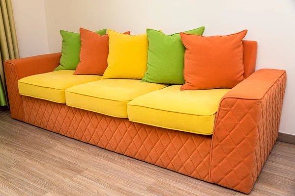 a colorful yellow-orange sofa with green, yellow and orange pillows