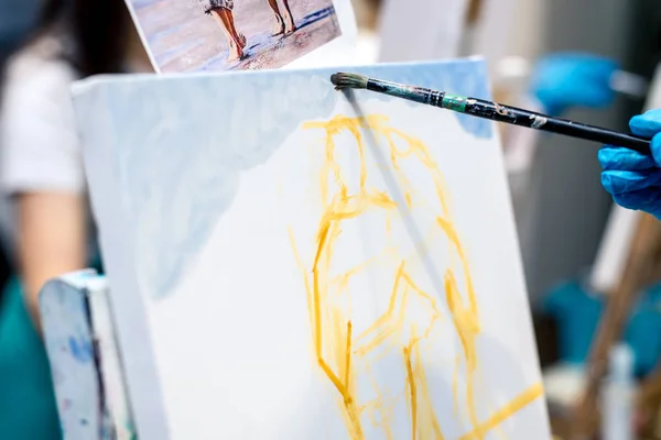 A painter's hand paints a multicolored drawing with a brush on a canvas. — Stock Photo, Image