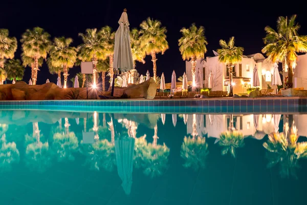 Paisagem noturna, interior do hotel com vista para a piscina, casas e palmeiras — Fotografia de Stock