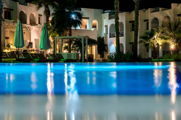 Paisagem noturna, interior do hotel com vista para a piscina, casas e palmeiras — Fotografia de Stock