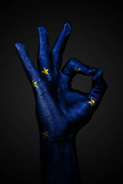 Una mano con una bandera de la UE dibujada muestra una señal aceptable sobre un fondo oscuro . — Foto de Stock